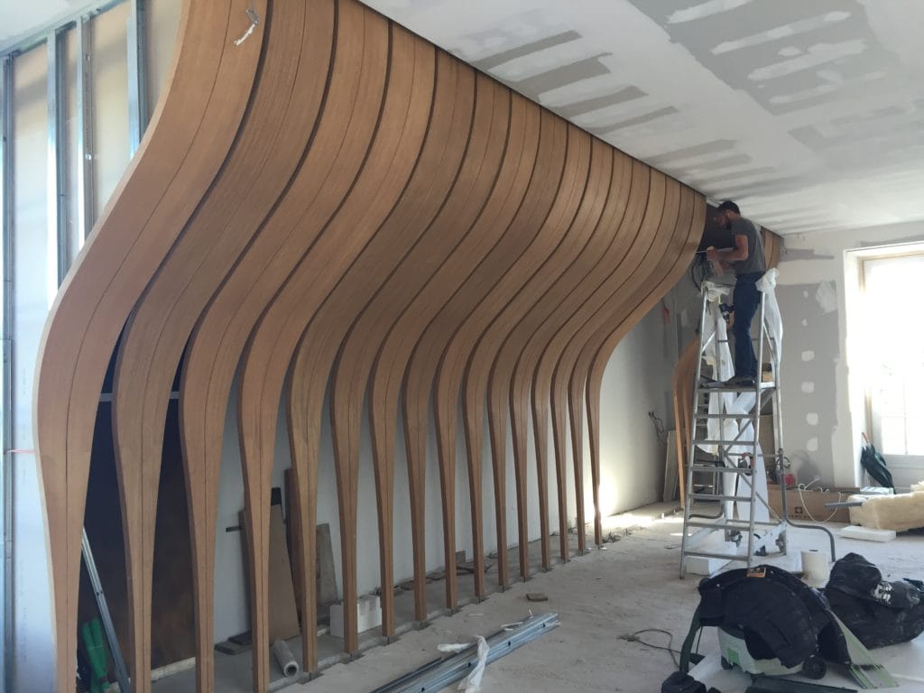 Photo de la pose des palmes de bois multiplis moulé pour la salle de présentation d'Yquem, on voit une personne les poser depuis un escabeau de chantier.